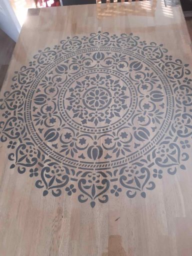 Dekoratives mandalaartiges Muster auf einem Holztisch in neutralen Farben.