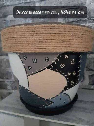 Gepflanzter Topf mit Patchwork-Muster in verschiedenen Farben und Holzdeckel.