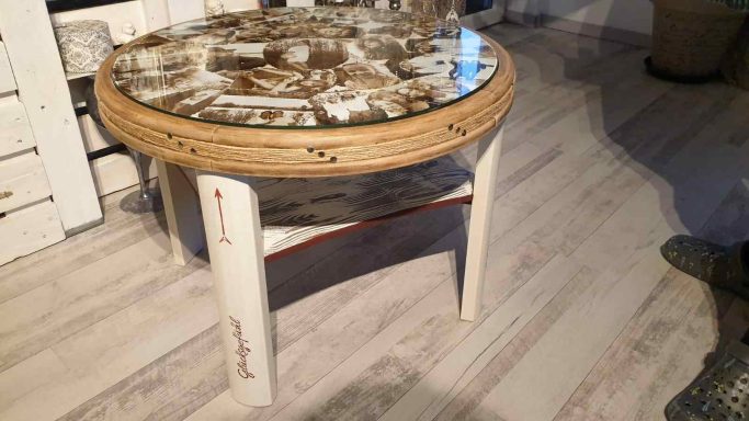 Runder Tisch mit einem dekorativen, detailreichen Glasoberteil und weißen Beinen.