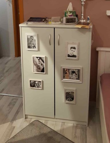 Schmaler Schrank mit Bildern auf der Vorderseite, in einem Zimmer mit rosa Wänden.