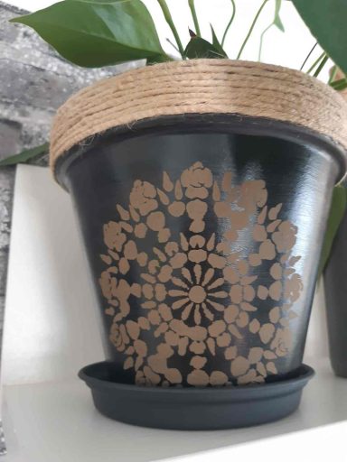 Schwarzer Blumentopf mit einem filigranen, goldenen Mandala-Muster und einem Untersetzer.