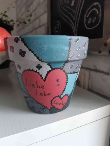 Bunter Blumentopf mit Herzmotiv und der Aufschrift "Liebe" in verschiedenen Farben.