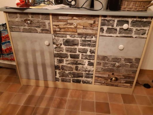 Schrank mit verschiedenen Oberflächen aus Stein, Holz und Metall in neutralen Farben.