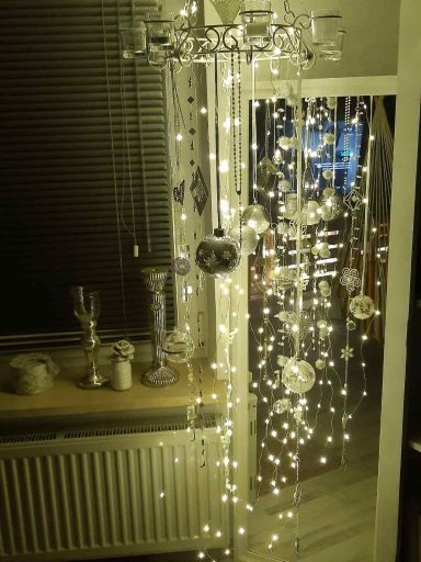 Lichterkette mit glitzernden Dekorationen hinter einem Fenster, warmes Licht.