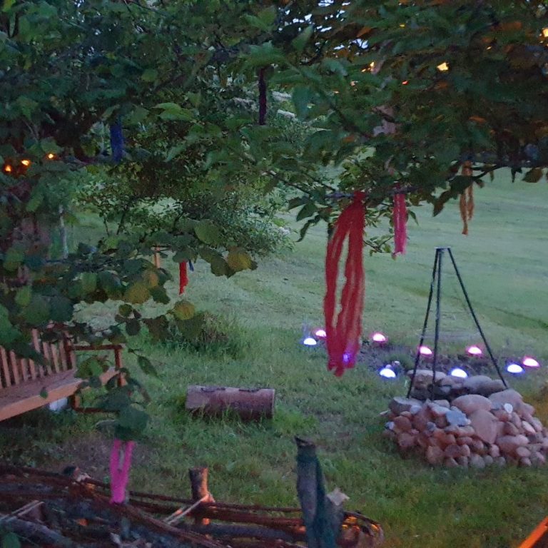 Licht-im-ich.de Gemütlicher Außenbereich mit bunten Bändern, Lichtern und einem Lagerfeuer.